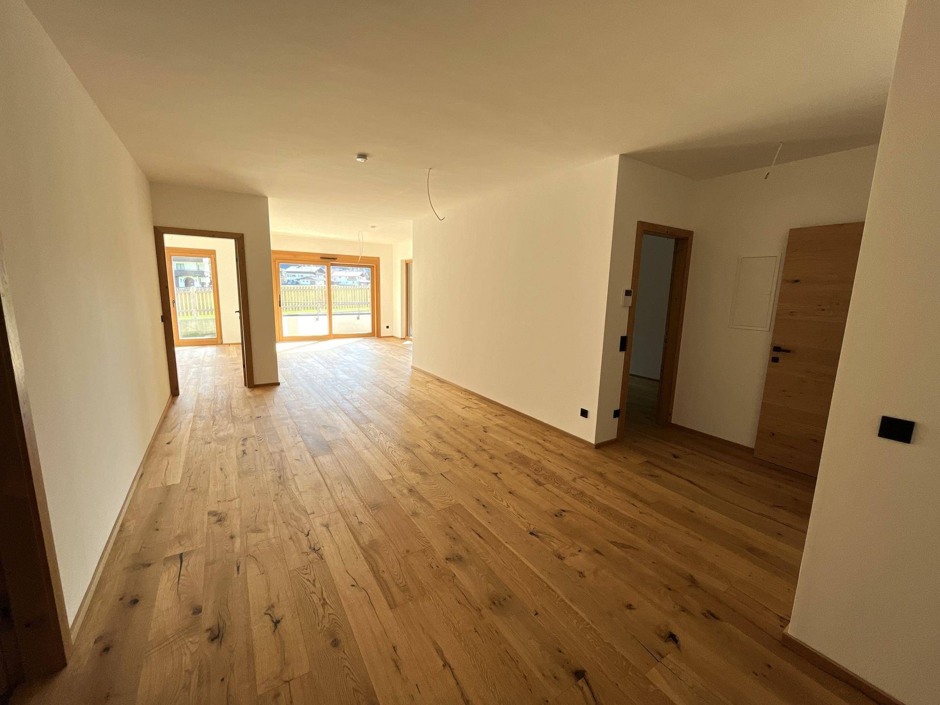 Geräumiger Wohnbereich mit hellem Holzboden und mehreren Türen, der viel Gestaltungspotenzial bietet.