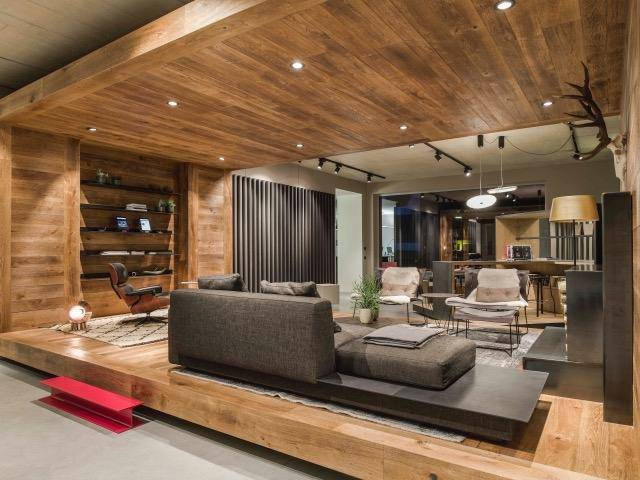 Geräumiger Wohnbereich mit Holzwänden und -decke, bequemen Sofas und integrierten Regalen.