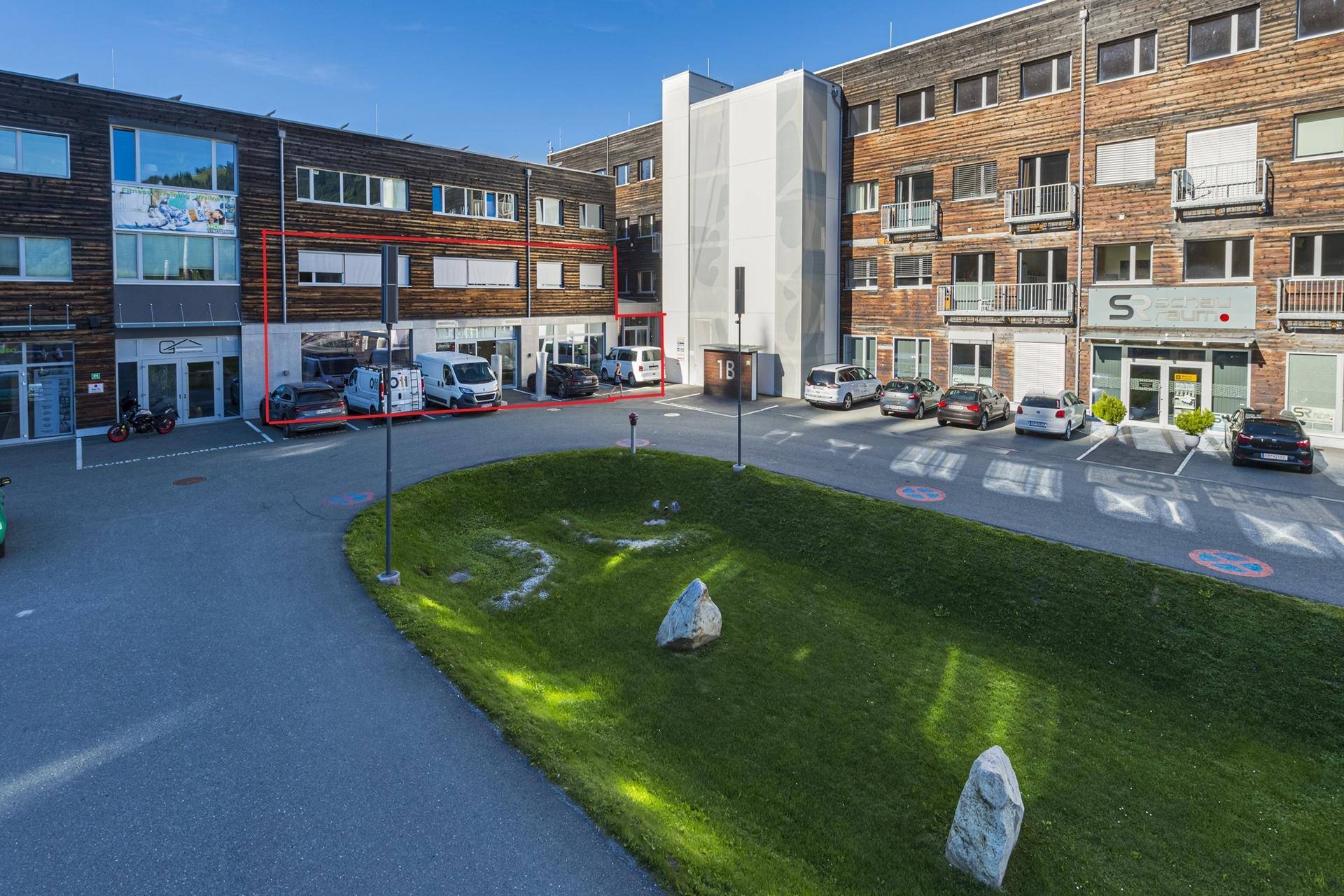 Ansicht eines modernen Gebäudes mit Holzfassade, Parkplätzen und hervorgehobener Geschäftsfläche.