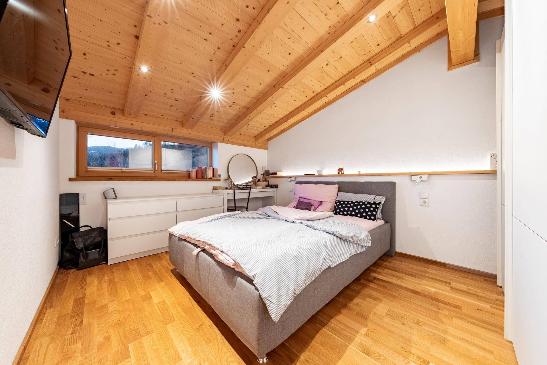 Schlafzimmer im Dachgeschoss mit Holzboden, schrägen Wänden und Fenster.