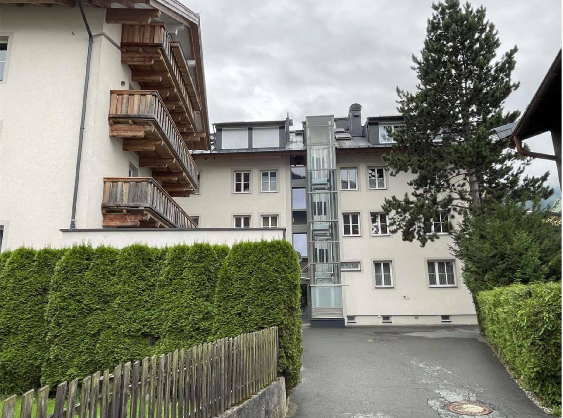 Mehrfamilienhaus mit externem Glasaufzug und gepflegter Hecke, bietet barrierefreien Zugang zu den Wohnungen.