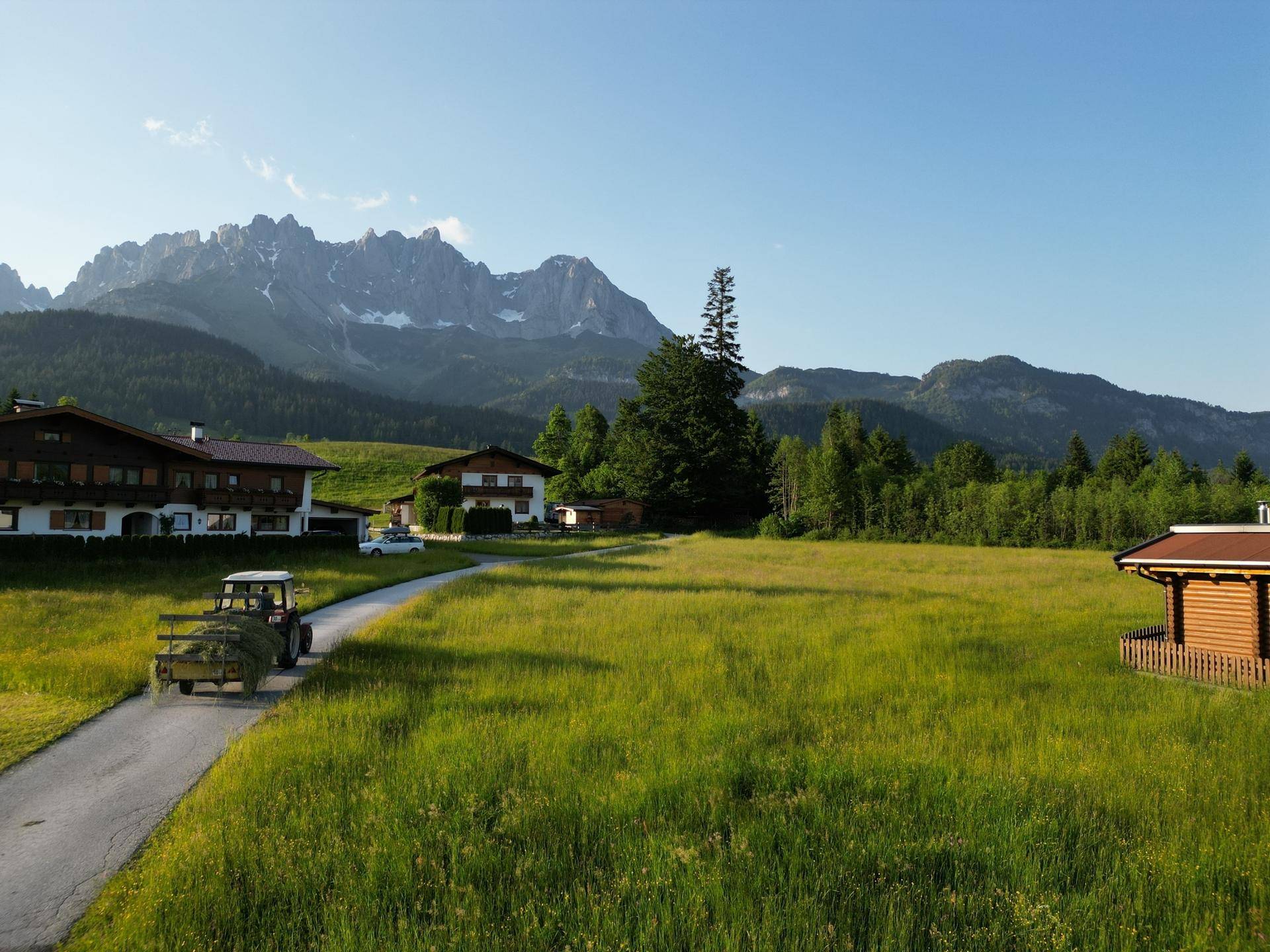 Ländliche Umgebung mit traditionellen Häusern, grünen Feldern und majestätischem Bergpanorama im Hintergrund.