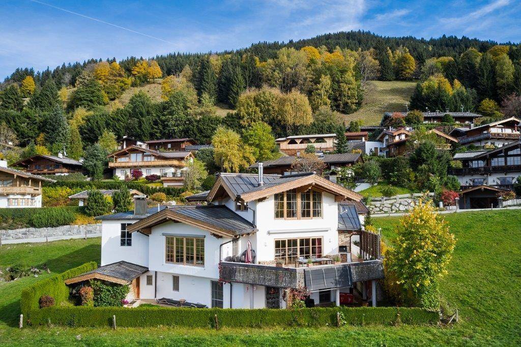 Großzügiges Alpenhaus in Hanglage mit mehreren Balkonen und weitem Blick über die grüne Landschaft.
