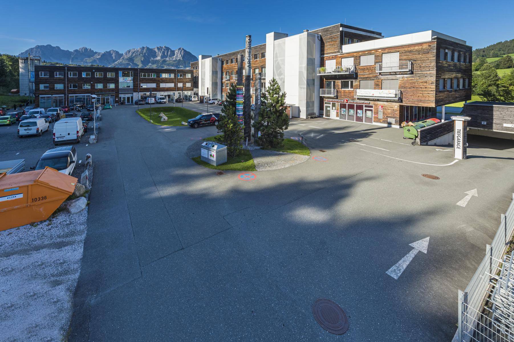 Weitläufiger Außenbereich eines modernen Gebäudekomplexes mit Parkplätzen und Bergblick.