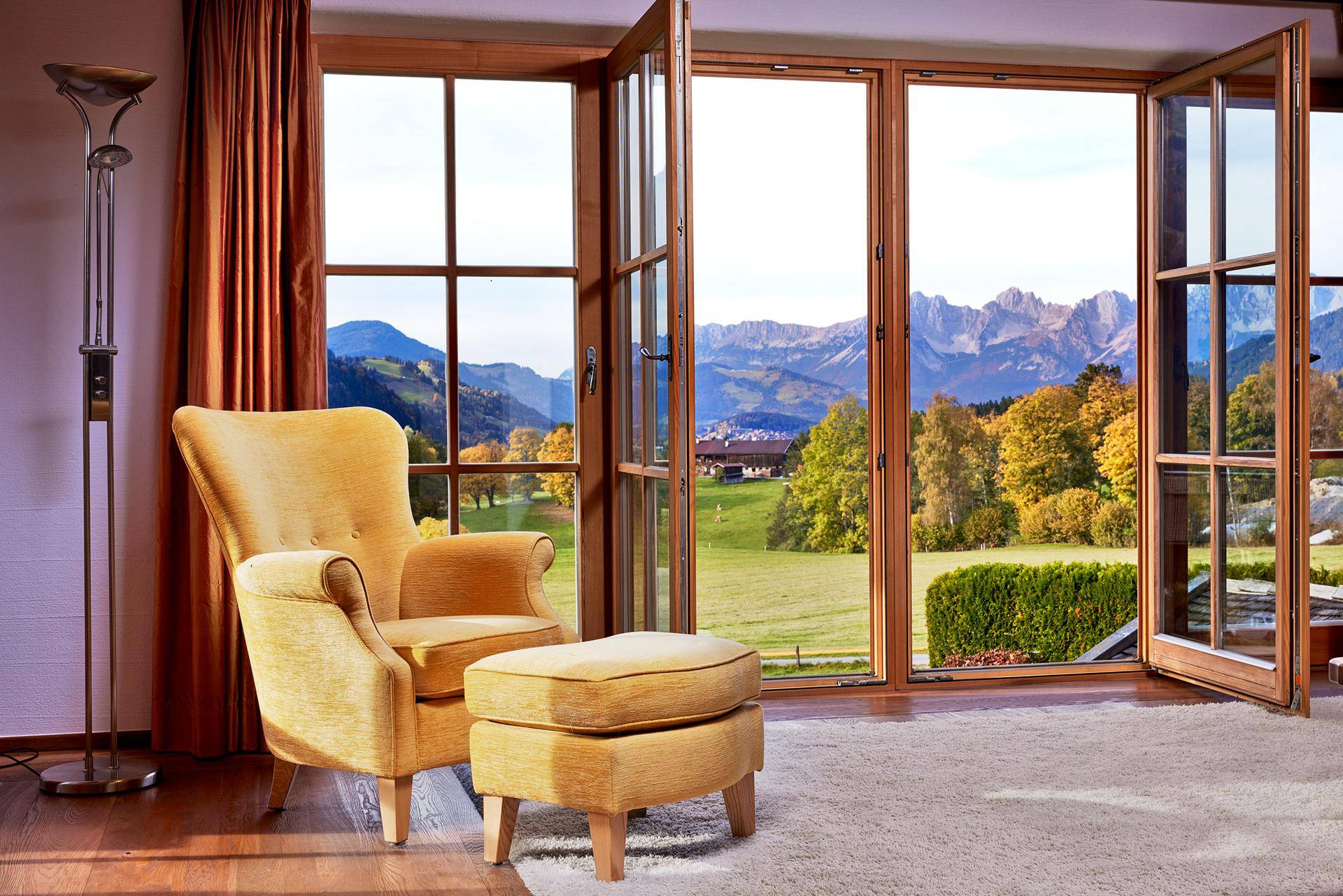 Gemütlicher Sessel am Fenster mit weitem Blick auf die grüne Landschaft und die Berge.