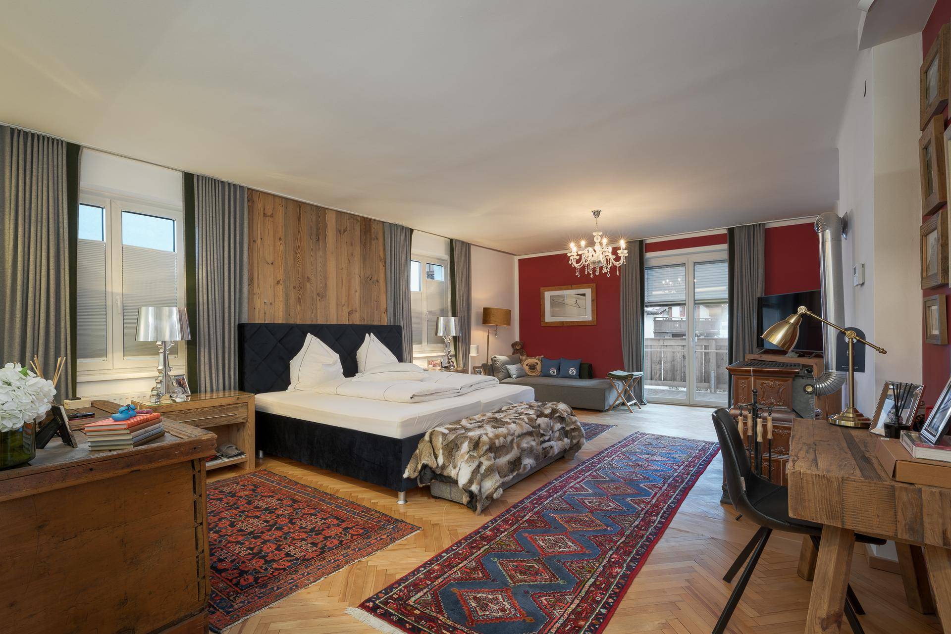 Großes Schlafzimmer mit Doppelbett, Sitzbereich und Schreibtisch, ausgestattet mit Holzboden und Teppichen.