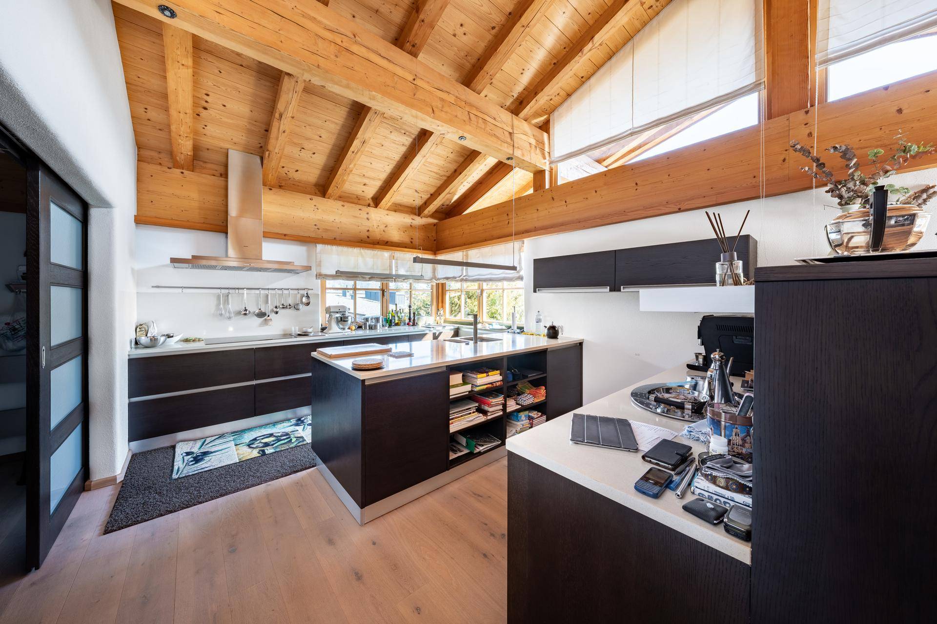Moderne Küche mit dunklen Schränken, Kücheninsel und Holzbalkendecke in offenem Design.