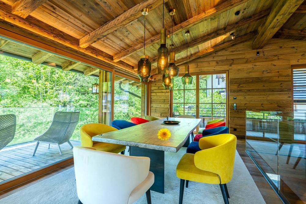 Heller Essbereich mit Holztisch, farbenfrohen Stühlen und Zugang zur Terrasse mit Waldblick.