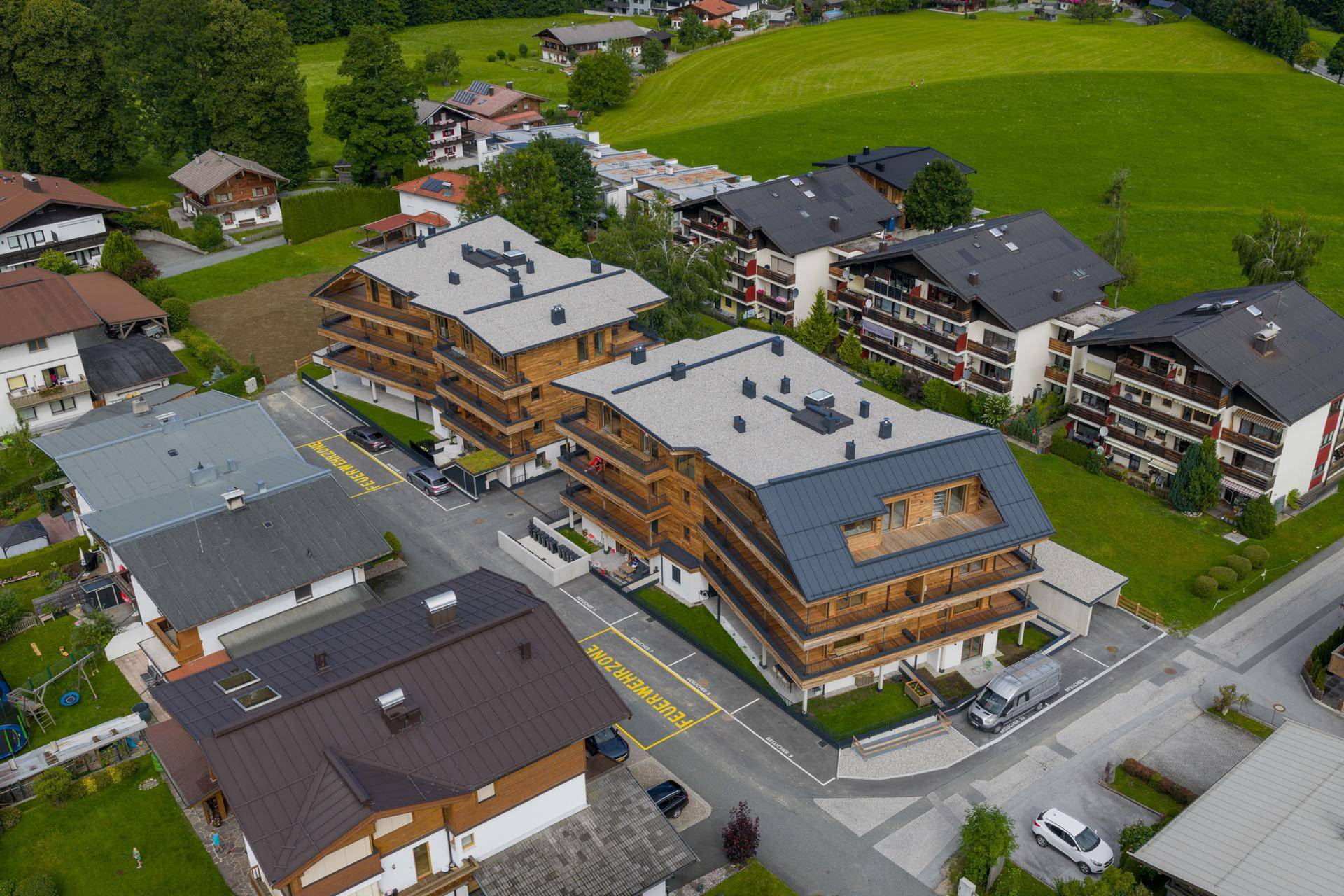 Vogelperspektive auf einen modernen Wohnkomplex mit Holzfassaden und Balkonen, eingebettet in eine ländliche Umgebung.