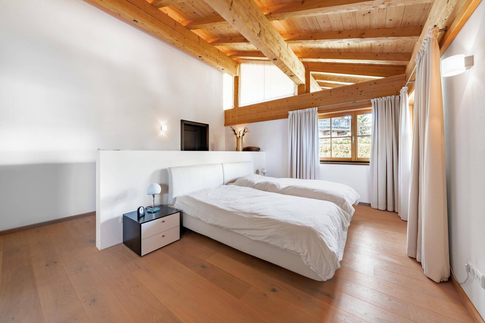 Helles Schlafzimmer mit Holzbalkendecke, Holzboden und großem Doppelbett.