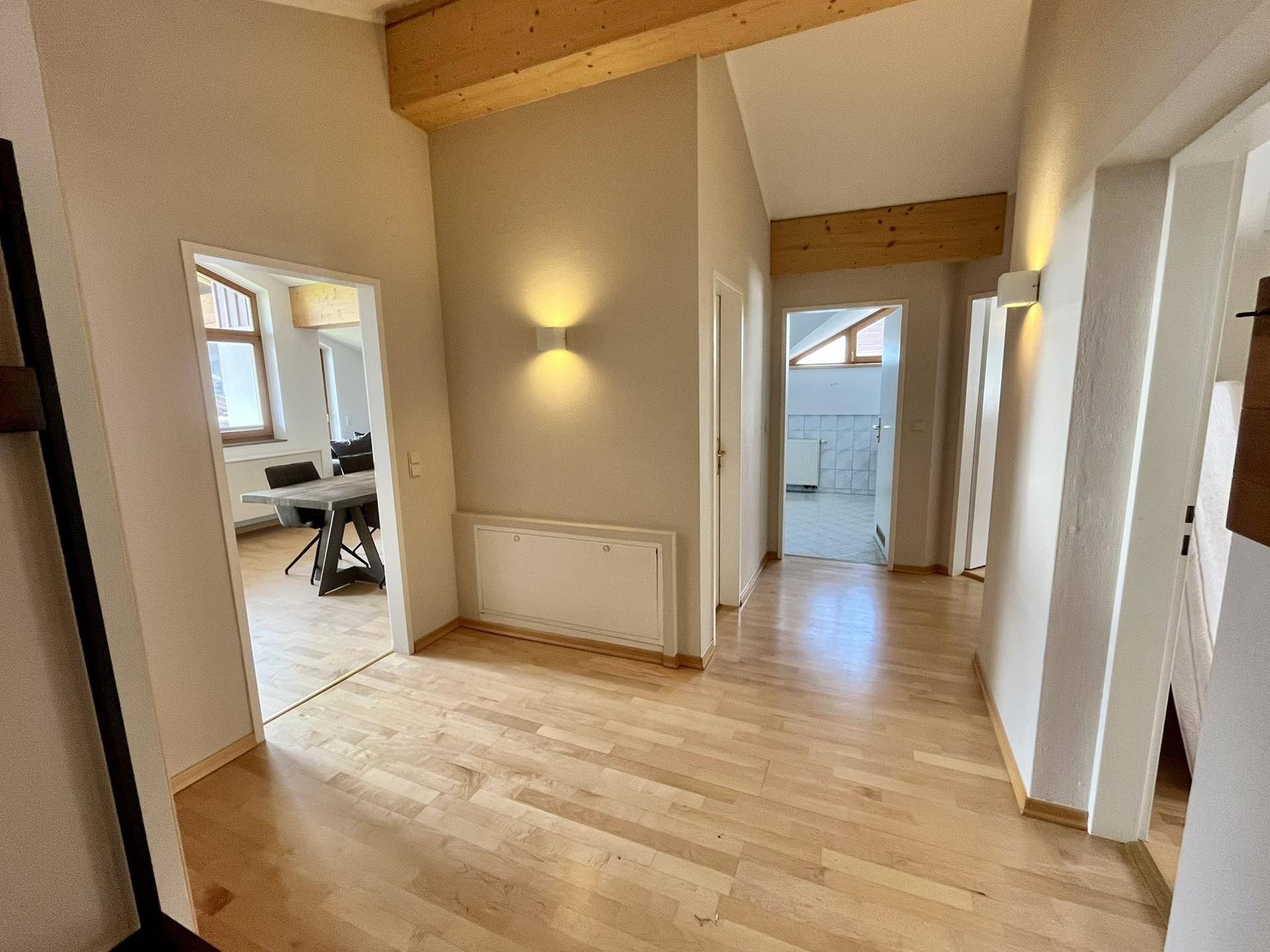 Heller Flur mit Holzboden und sichtbaren Holzbalken, der zu verschiedenen Räumen führt.