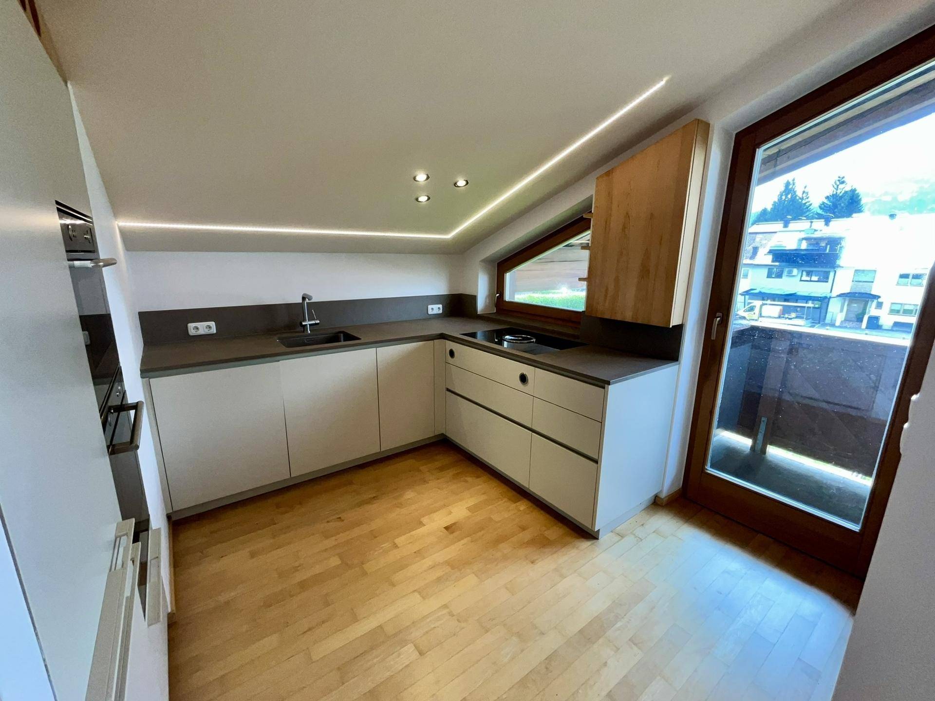 Moderne Küche mit weißen Schränken, dunkler Arbeitsplatte und Zugang zu einem Balkon oder Terrasse.