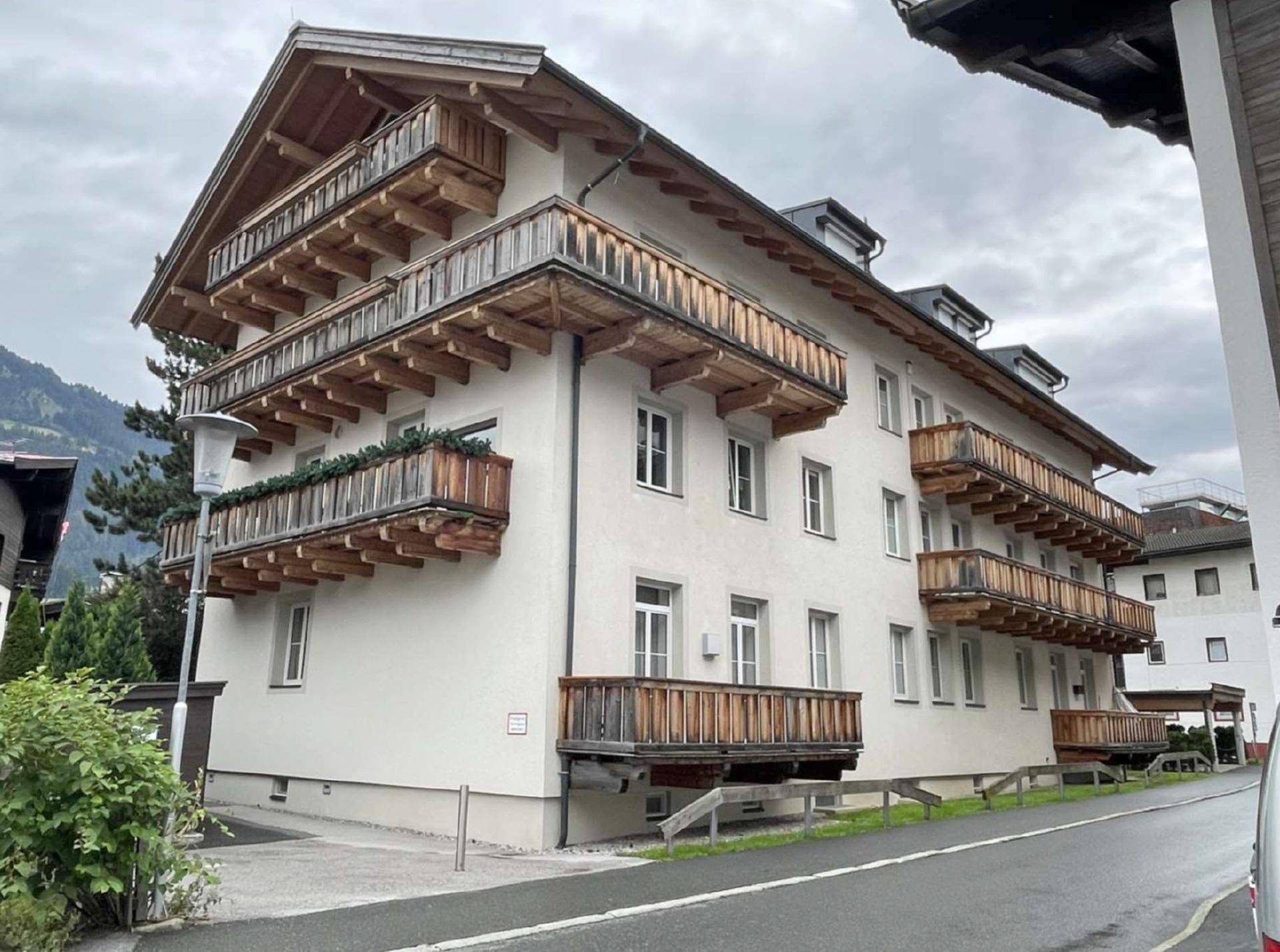 Traditionelles Mehrfamilienhaus mit vielen Holzbalkonen und weißer Fassade, eingebettet in die alpine Umgebung.