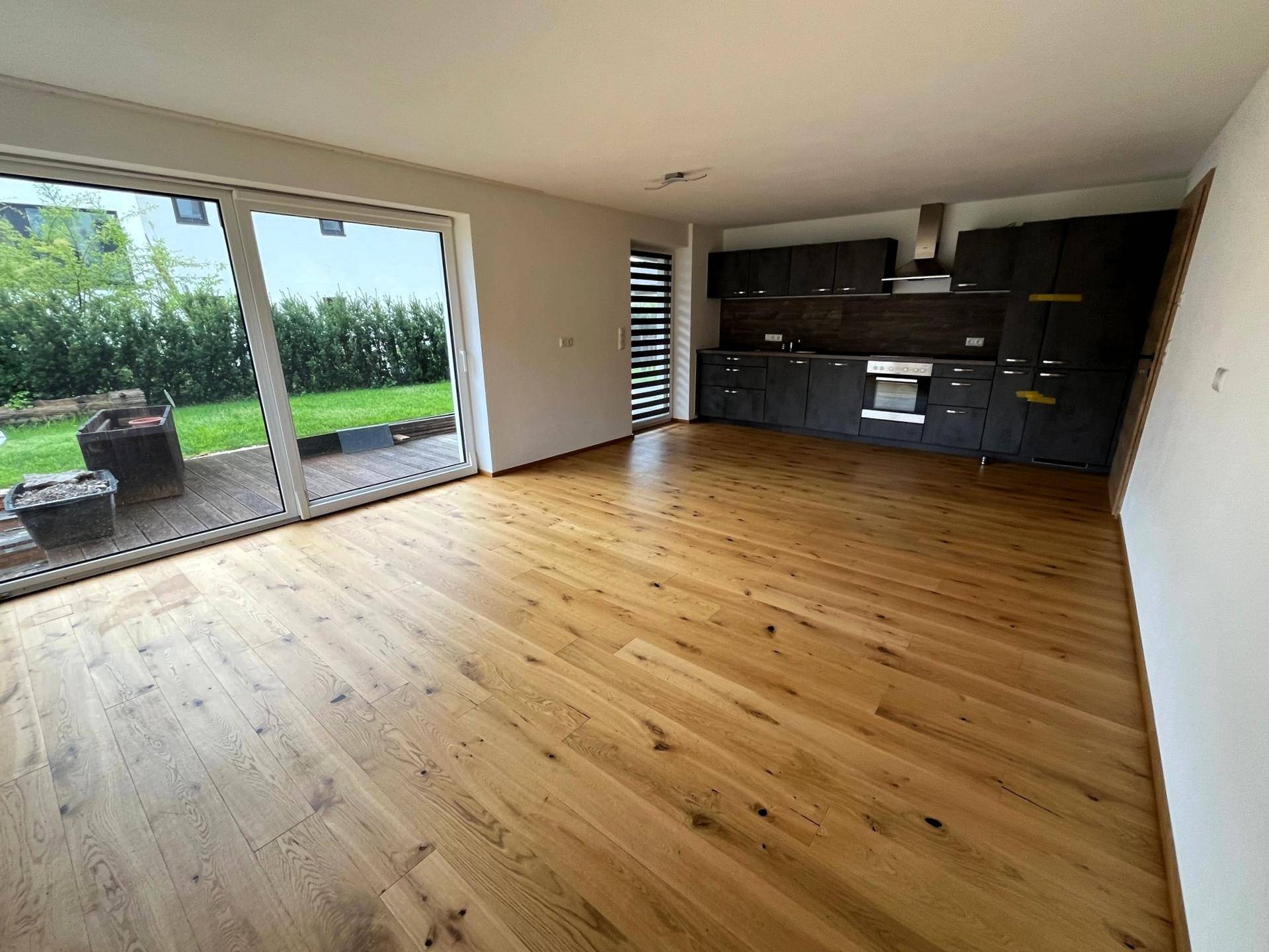 Offener Wohnbereich mit Holzboden und integrierter Küche, mit Zugang zur Terrasse und Garten.