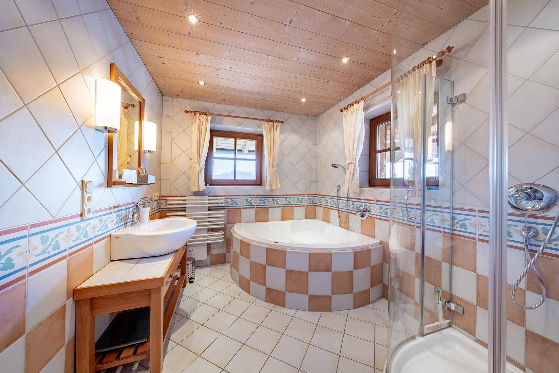 Badezimmer mit Eckbadewanne, Dusche, Fenster und traditionellen Fliesen in warmen Farben und Mustern.