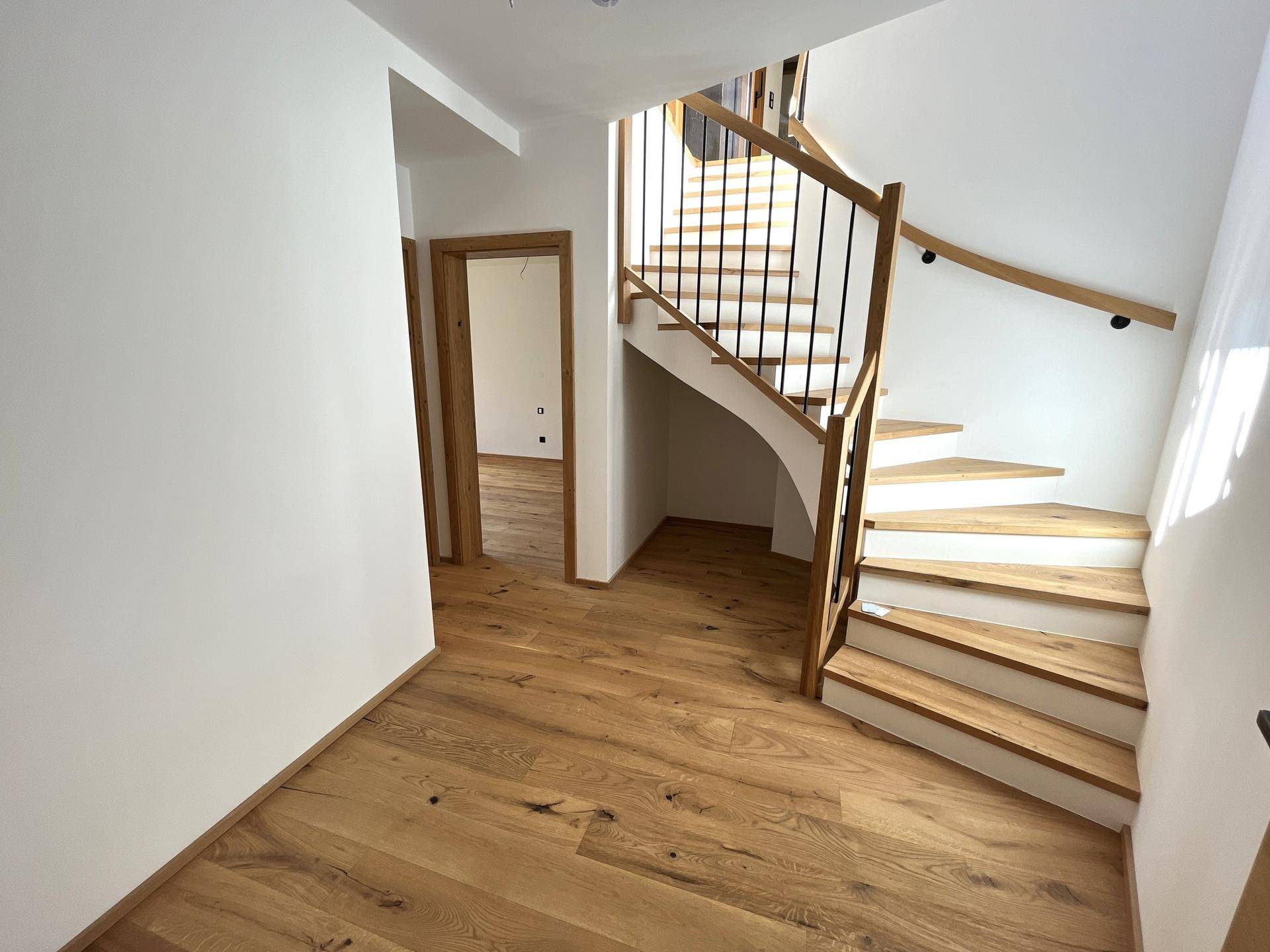 Heller Eingangsbereich mit Holztreppe, Parkettboden und Zugang zu weiteren Räumen.