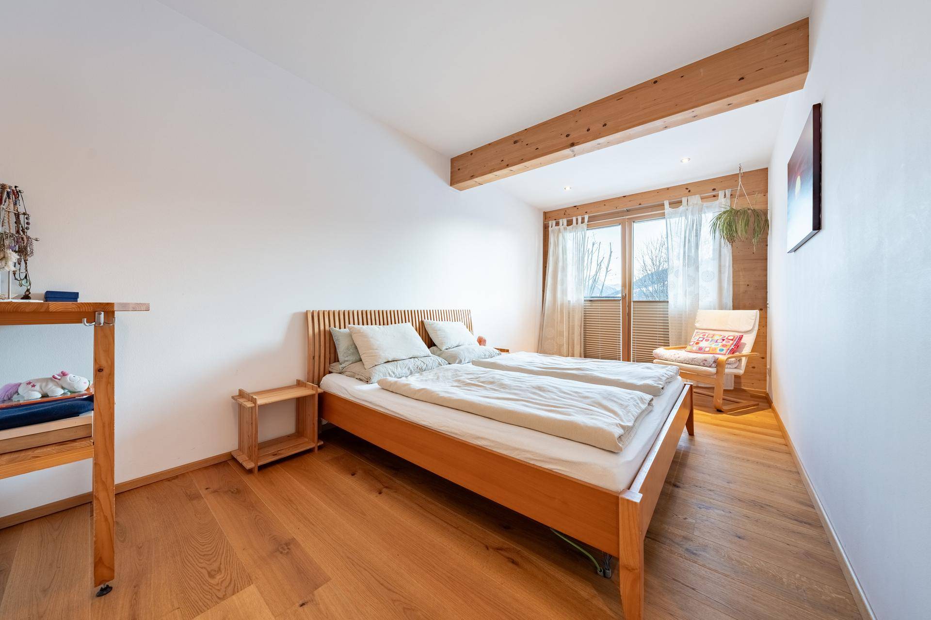 Helles Schlafzimmer mit Holzboden, Holzbalken und Fenster mit Blick ins Grüne.