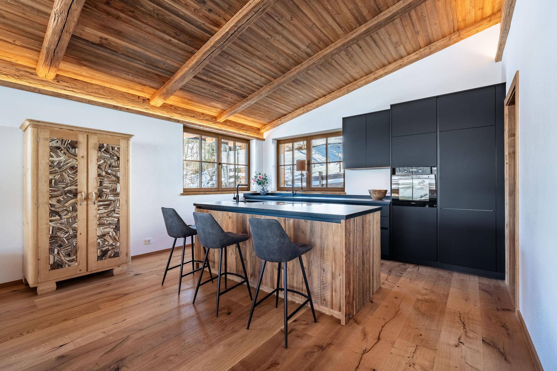 Moderne Küche mit schwarzen Schränken, Holzinsel und rustikalem Holzschrank im alpinen Stil.