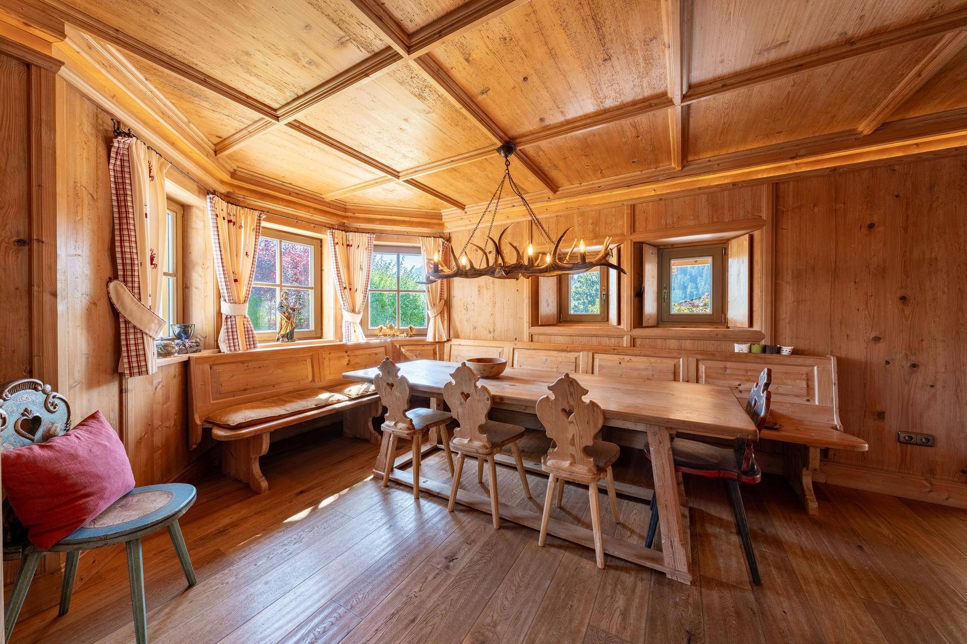 Traditioneller Essbereich mit Holztäfelung, Holzboden und einem großen Esstisch mit Bänken und Geweihleuchter.