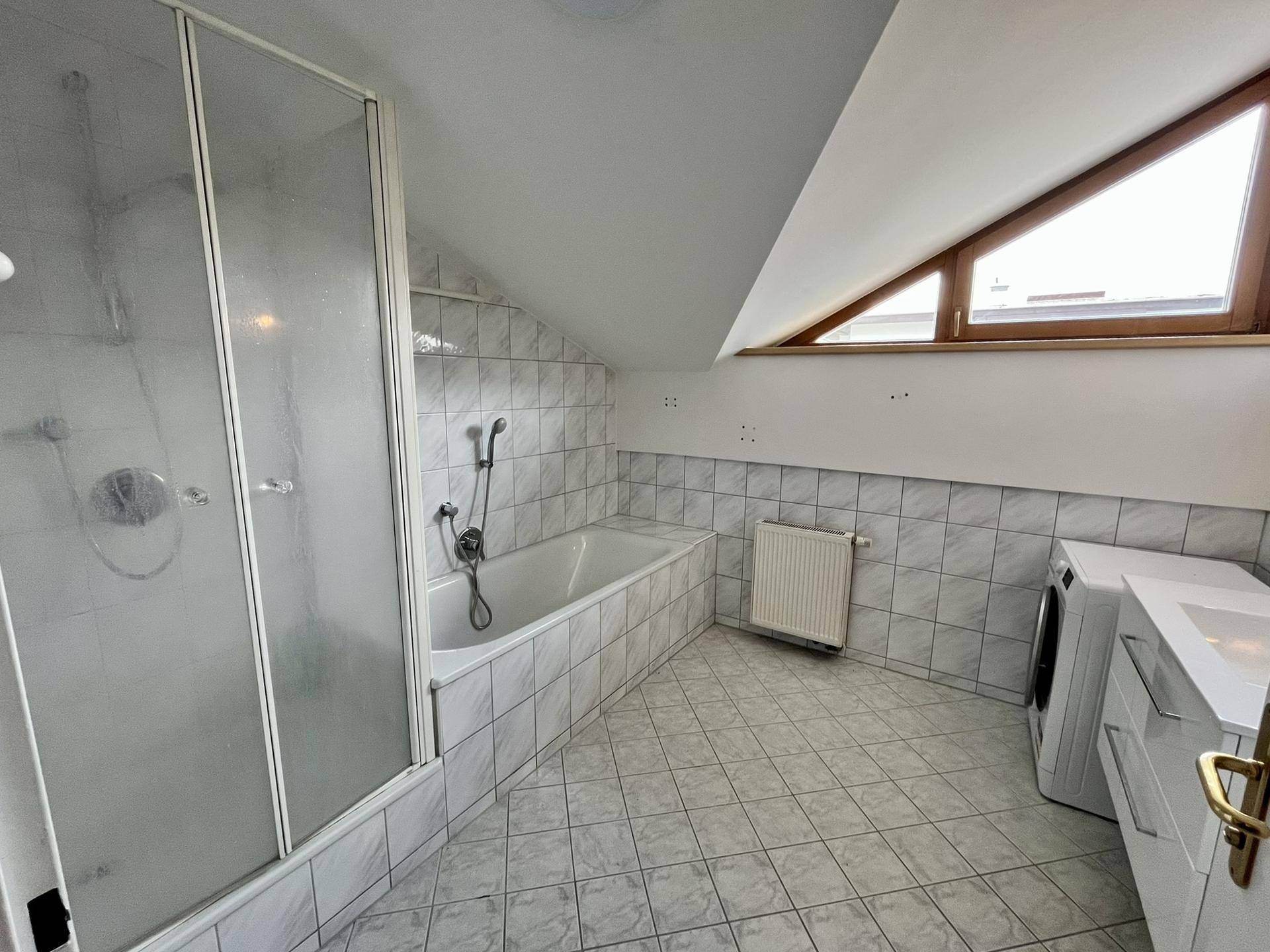 Badezimmer mit Badewanne, Dusche, Waschmaschine und Dachschräge mit Fenster.