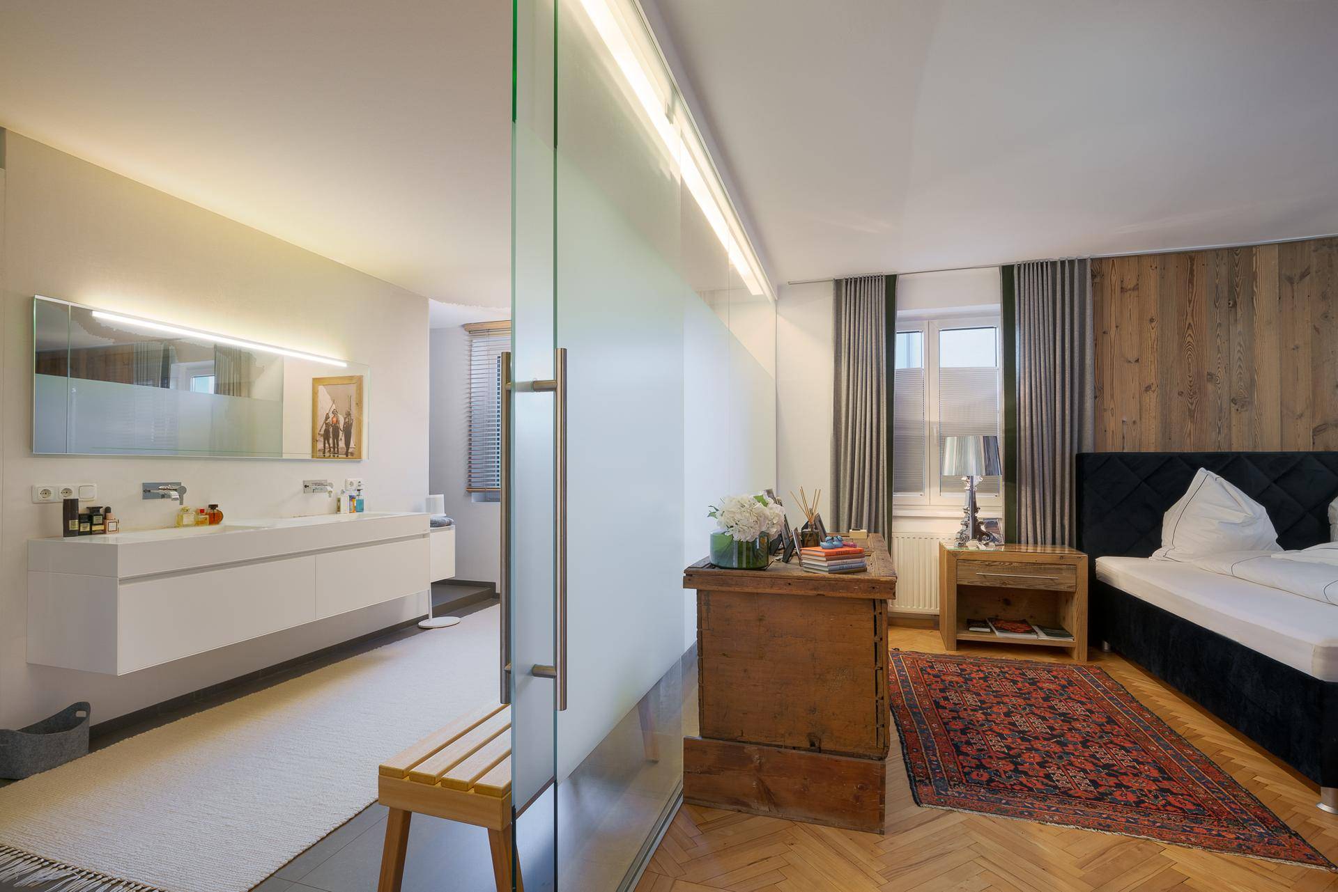 Geräumiges Schlafzimmer mit Holzboden und offenem Zugang zu einem modernen Badezimmer mit Doppelwaschbecken.