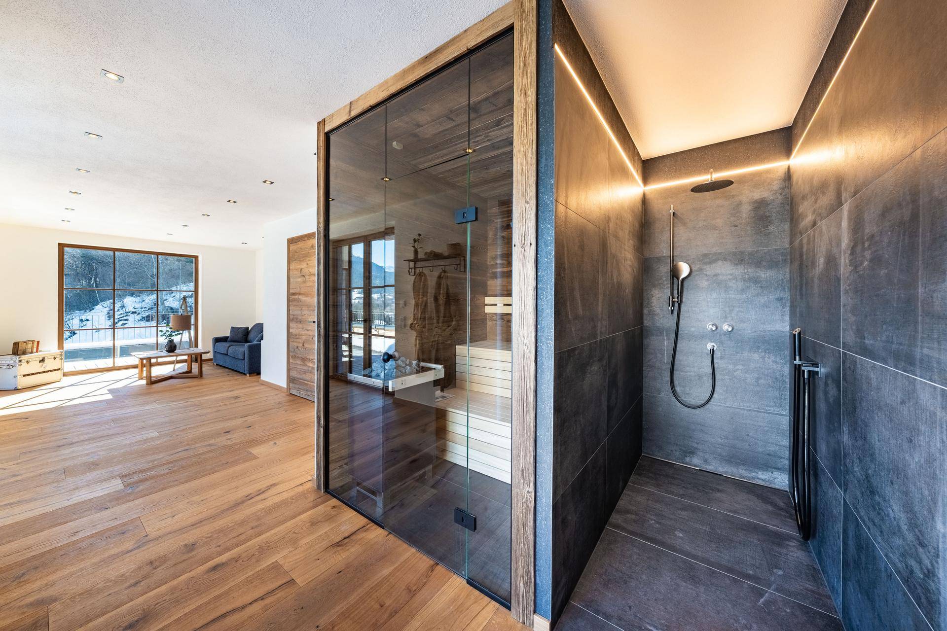Exklusiver Wellnessbereich mit Glas-Sauna, moderner Regendusche und Holzboden.