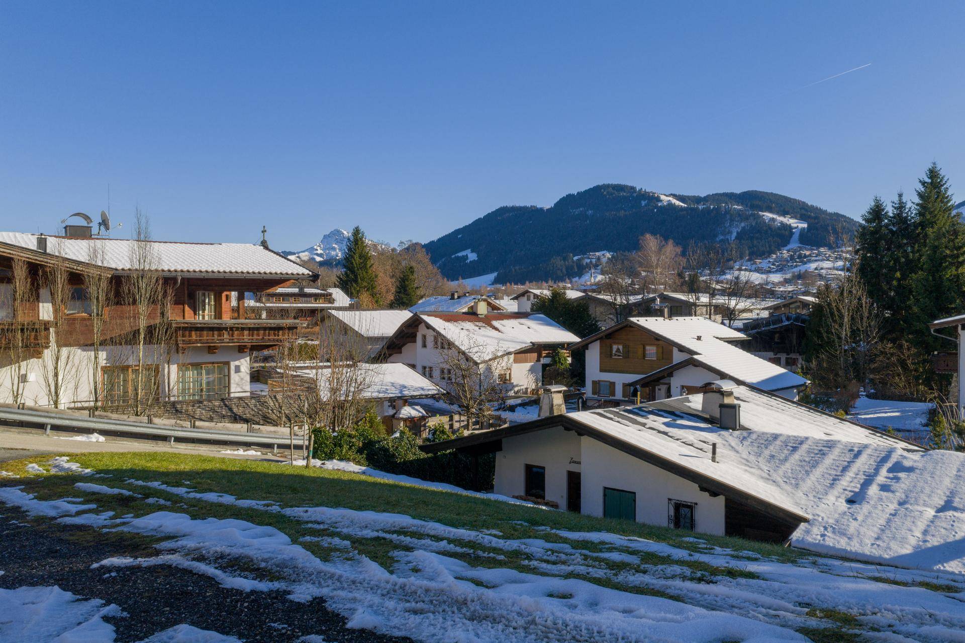 Weitläufiger Blick auf eine Siedlung mit schneebedeckten Dächern und einer beeindruckenden Bergkulisse.