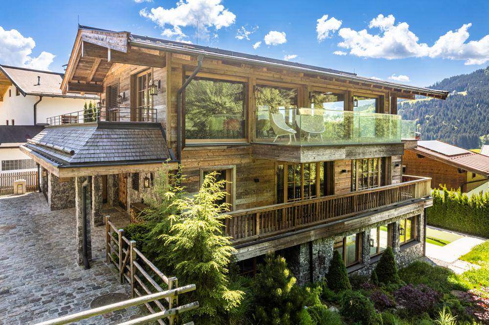 Elegantes Holzchalet mit Steinakzenten, großen Glasfronten und Balkonen vor einer malerischen Bergkulisse.