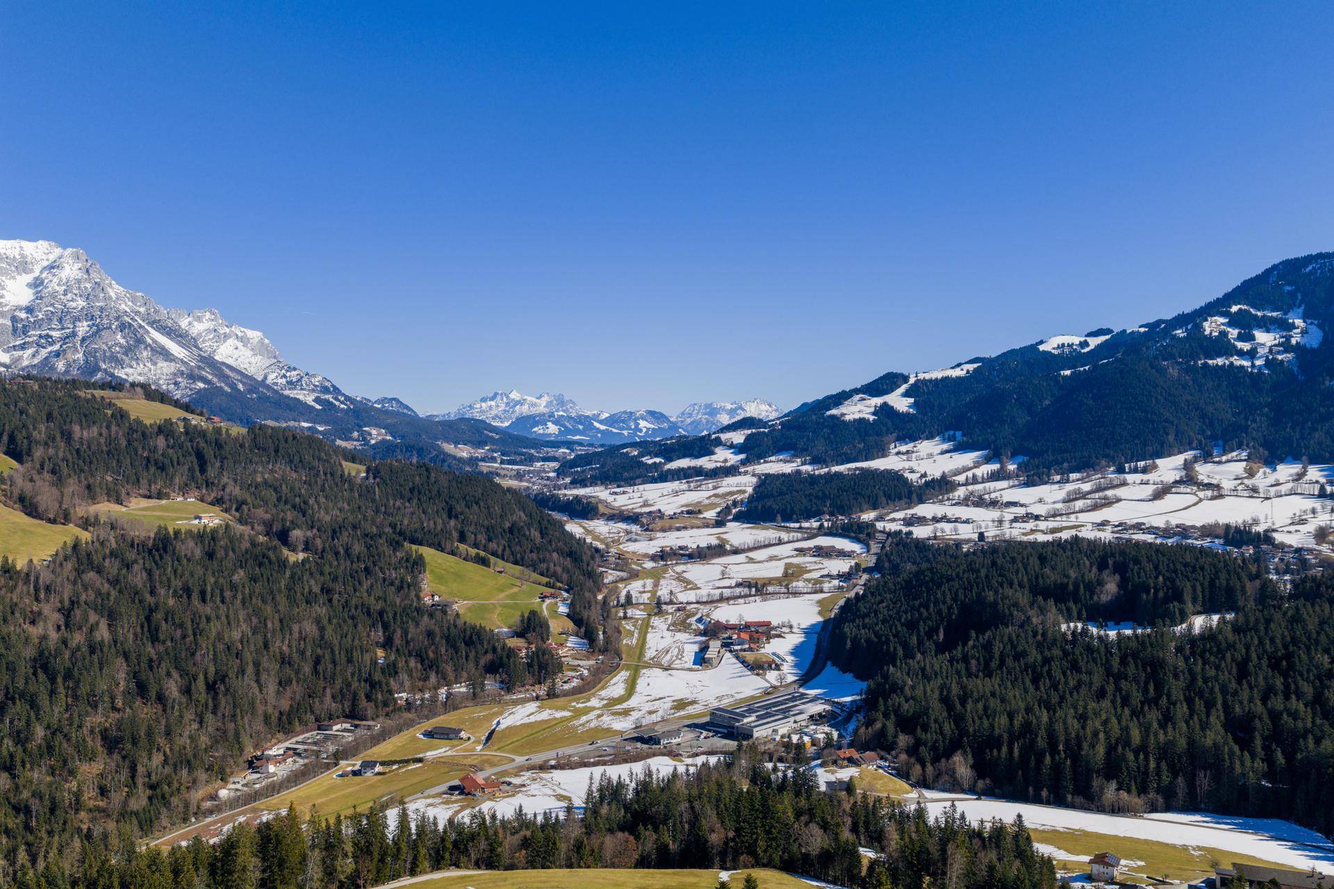 Atemberaubende Panoramaansicht eines weiten Alpentals mit schneebedeckten Gipfeln und dichten Wäldern.