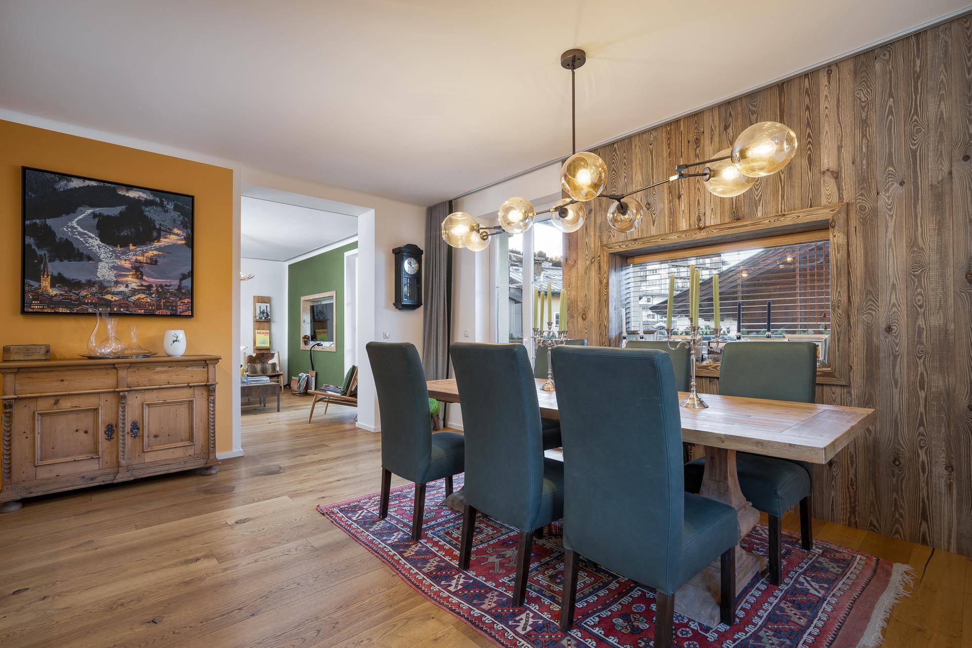 Rustikaler Essbereich mit großem Holztisch, bequemen Stühlen und Holzwandverkleidung, verbunden mit dem Wohnzimmer.