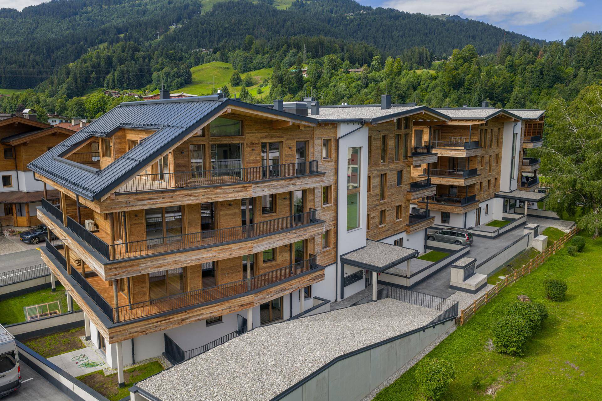 Neubau-Apartmenthaus mit Holzfassade und mehreren Balkonen, eingebettet in eine grüne Hügellandschaft.