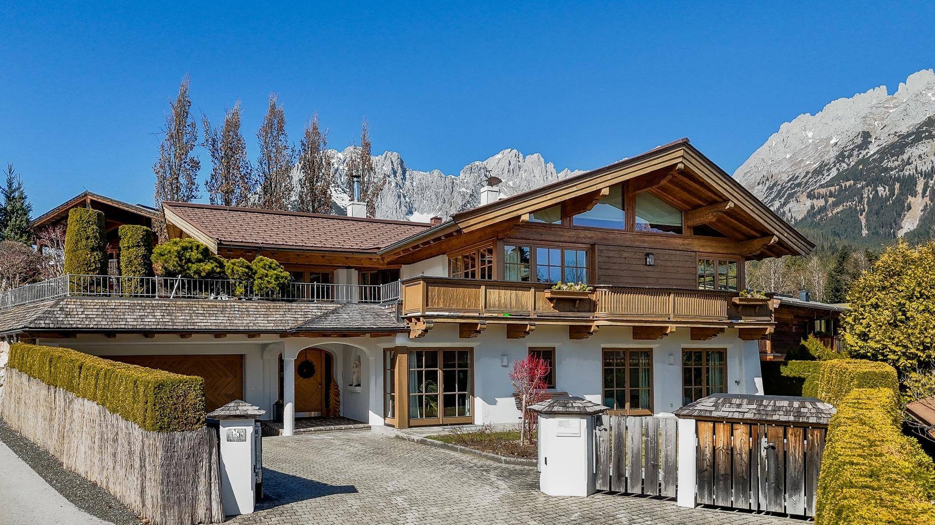 Charmantes Alpenchalet mit Holzbalkonen und gepflasterter Auffahrt vor majestätischer Bergkulisse.