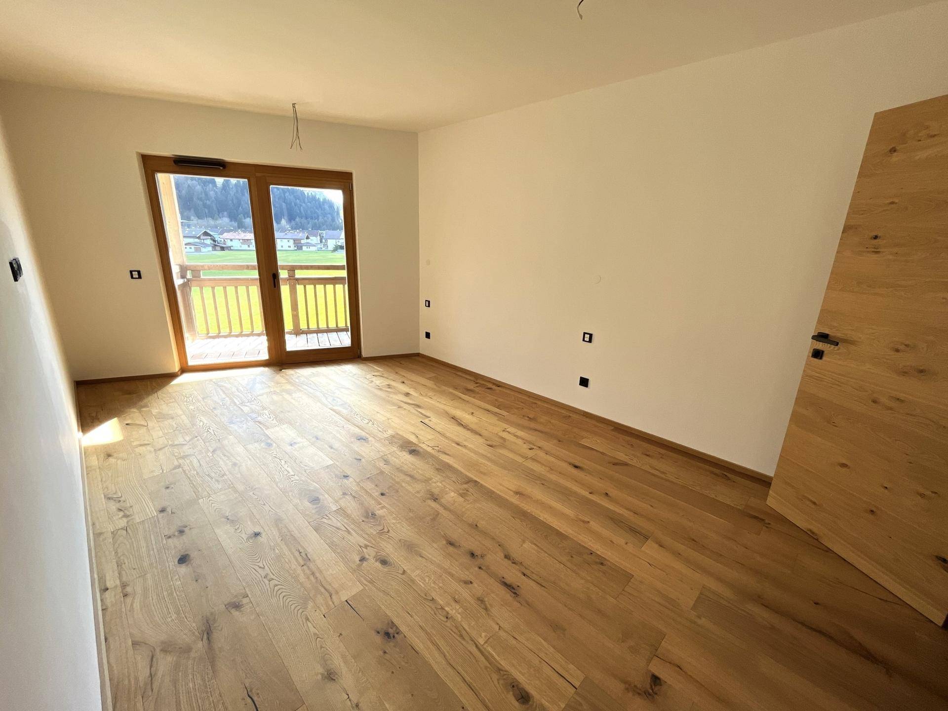 Helles Schlafzimmer mit Holzboden und Zugang zu einem Balkon mit Bergblick.