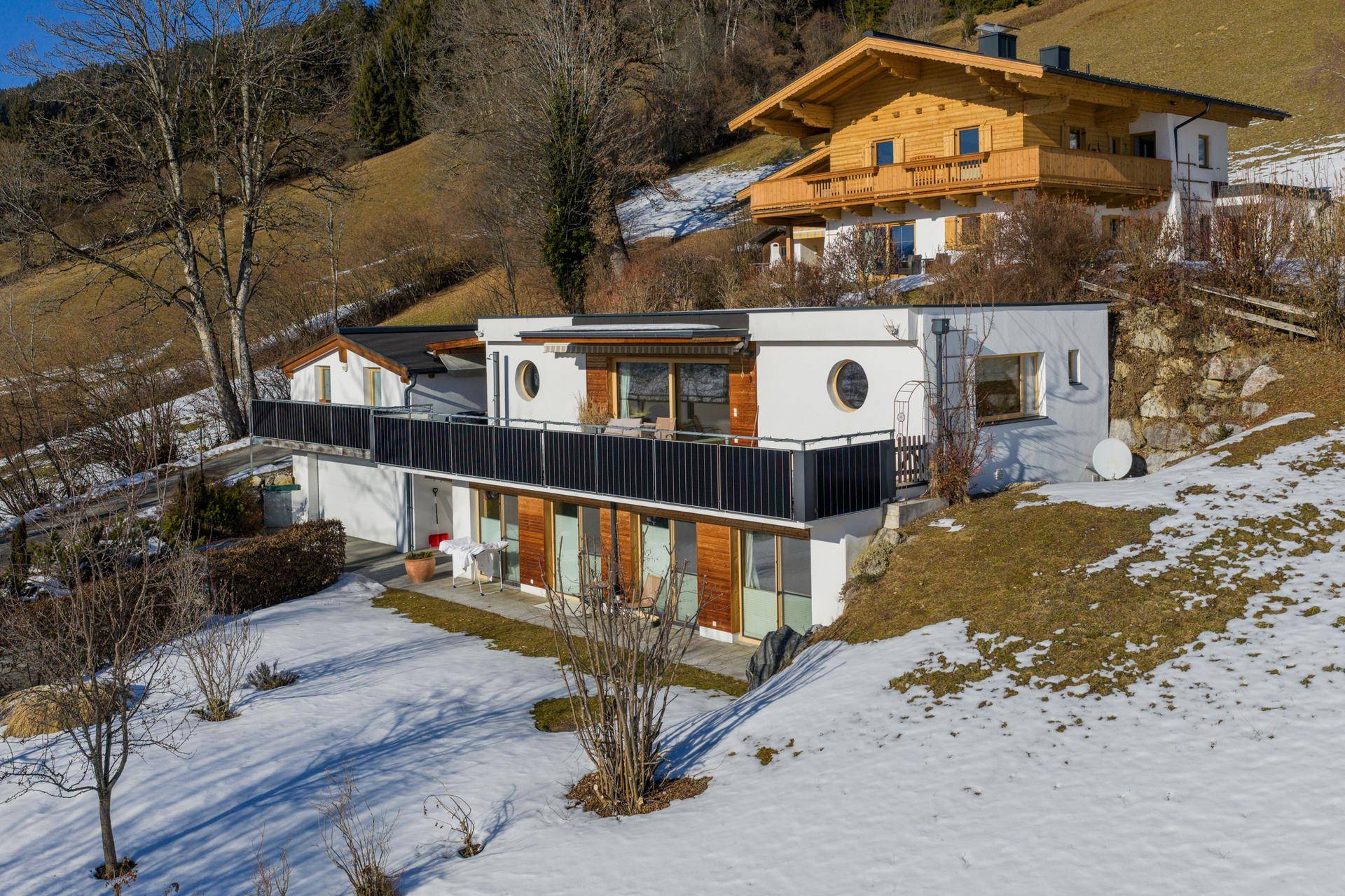 Modernes Haus mit Balkonen und Terrassen in einer verschneiten Berglandschaft.