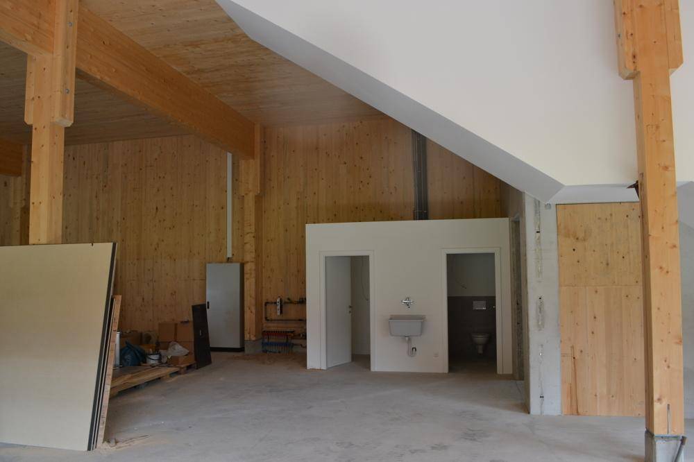 Großer Raum im Bau mit Holzverkleidung, sichtbaren Balken und einem teilweise fertigen Sanitärbereich.