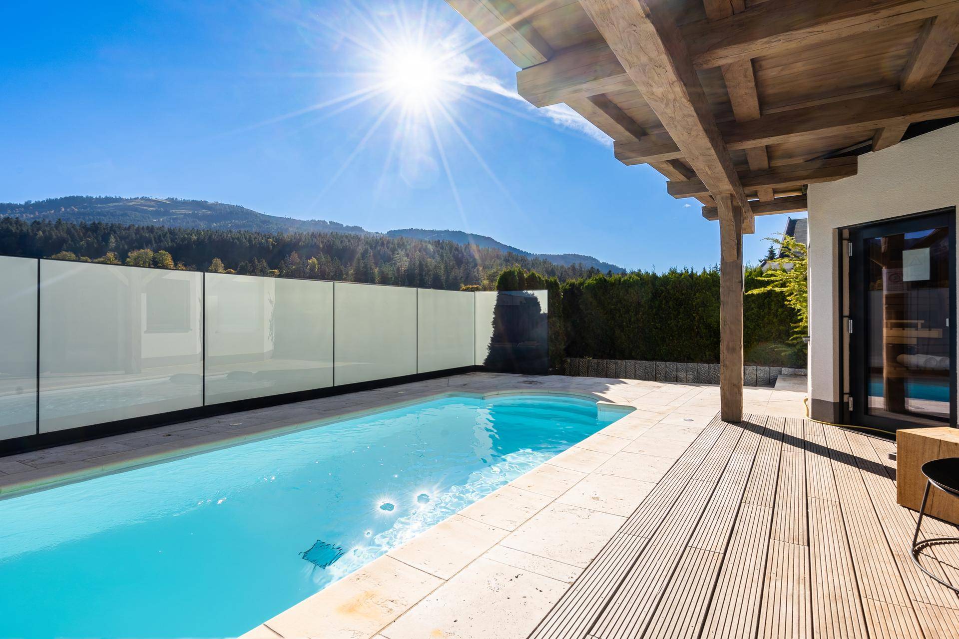 Sonniger Außenpool mit Holzdeck und Bergblick, umgeben von grüner Natur.