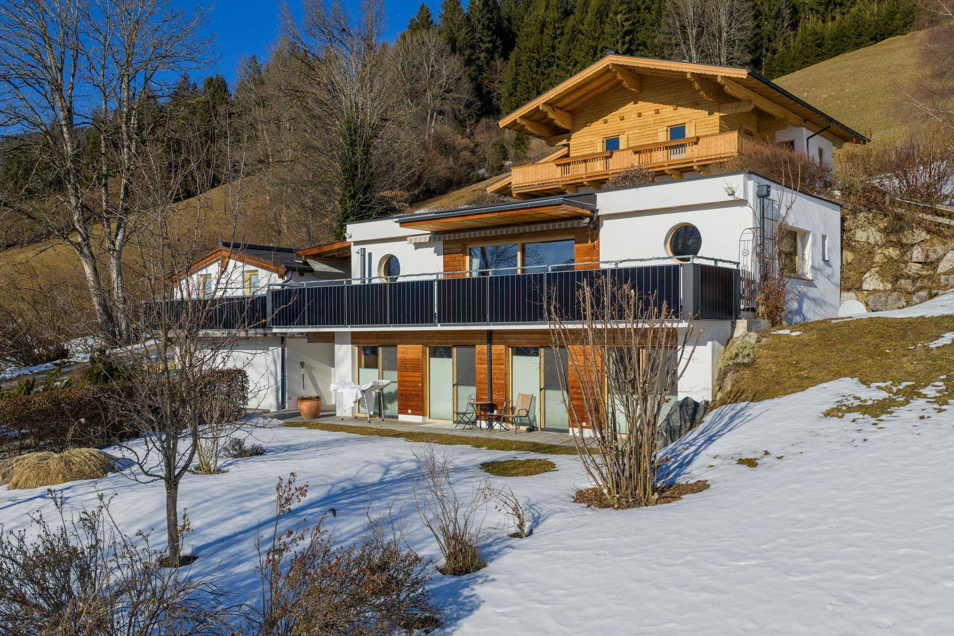 Das moderne Wohnhaus mit großen Fenstern und Balkonen, eingebettet in eine winterliche Bergkulisse.