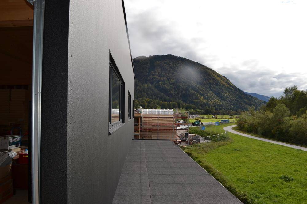 Blick von einem Balkon auf eine weite grüne Landschaft mit bewaldeten Bergen unter bewölktem Himmel.