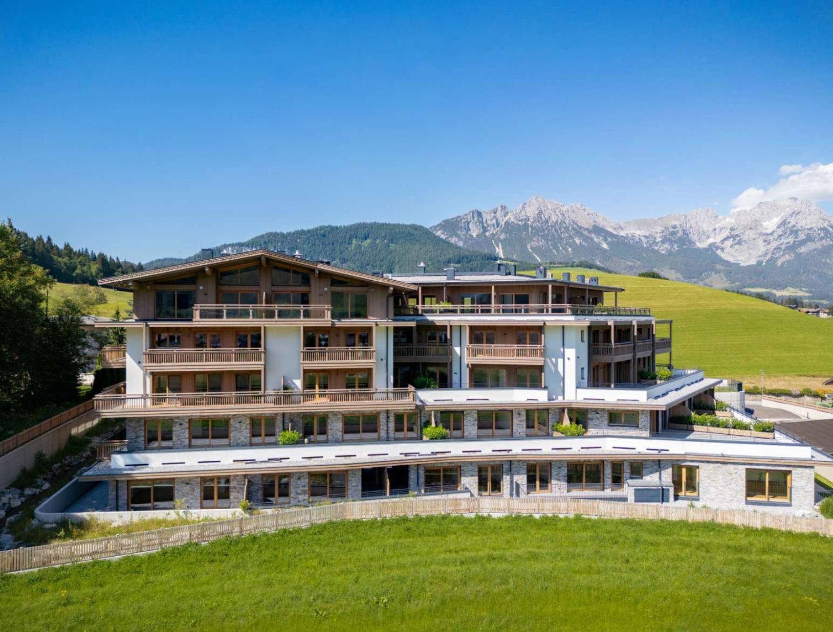 Modernes Wohngebäude in den Alpen mit Panoramablick auf Berge und grüne Wiesen.