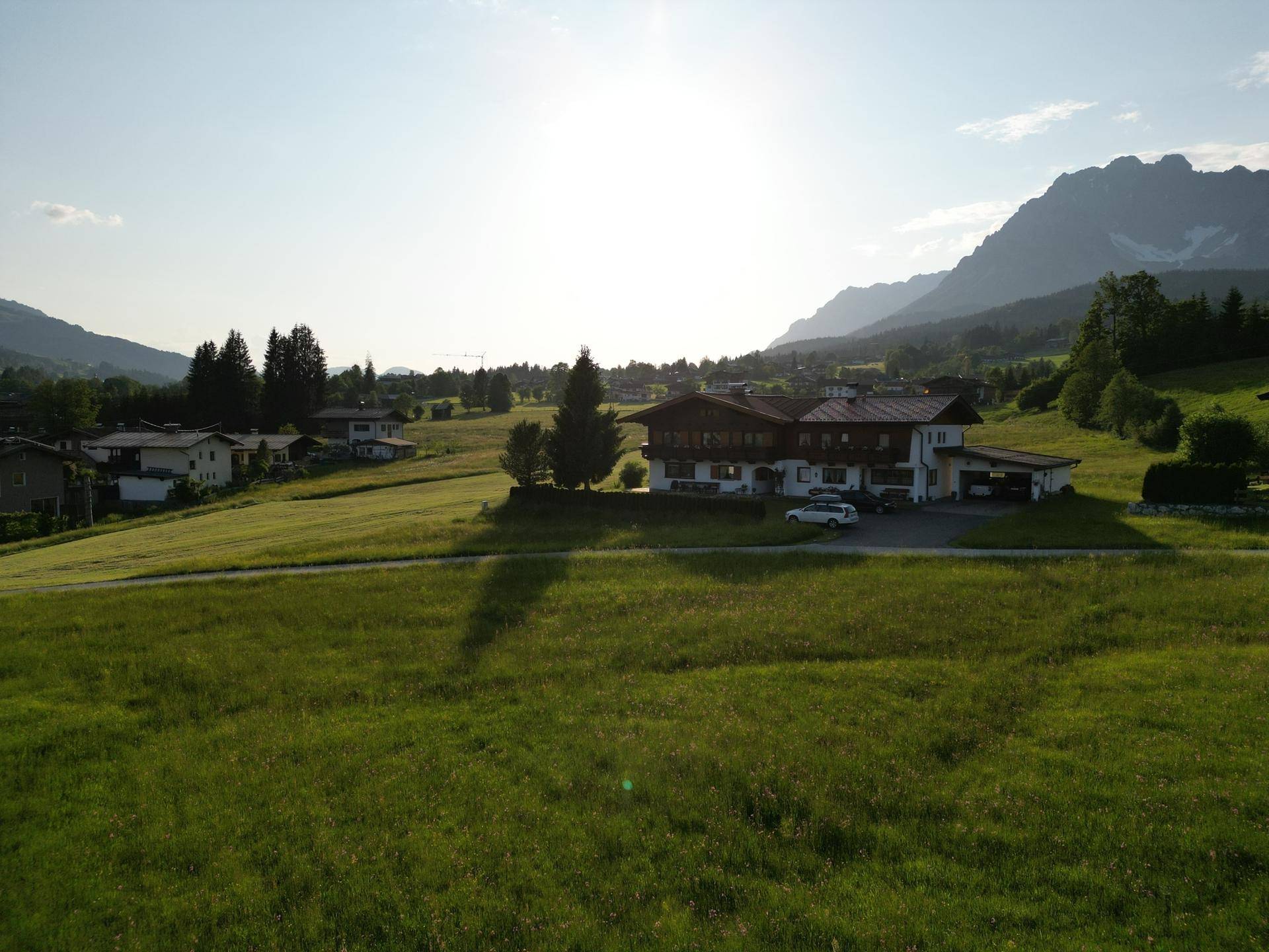 Haus in sonniger ländlicher Lage, umgeben von grünen Wiesen mit Blick auf die umliegende Bergwelt.