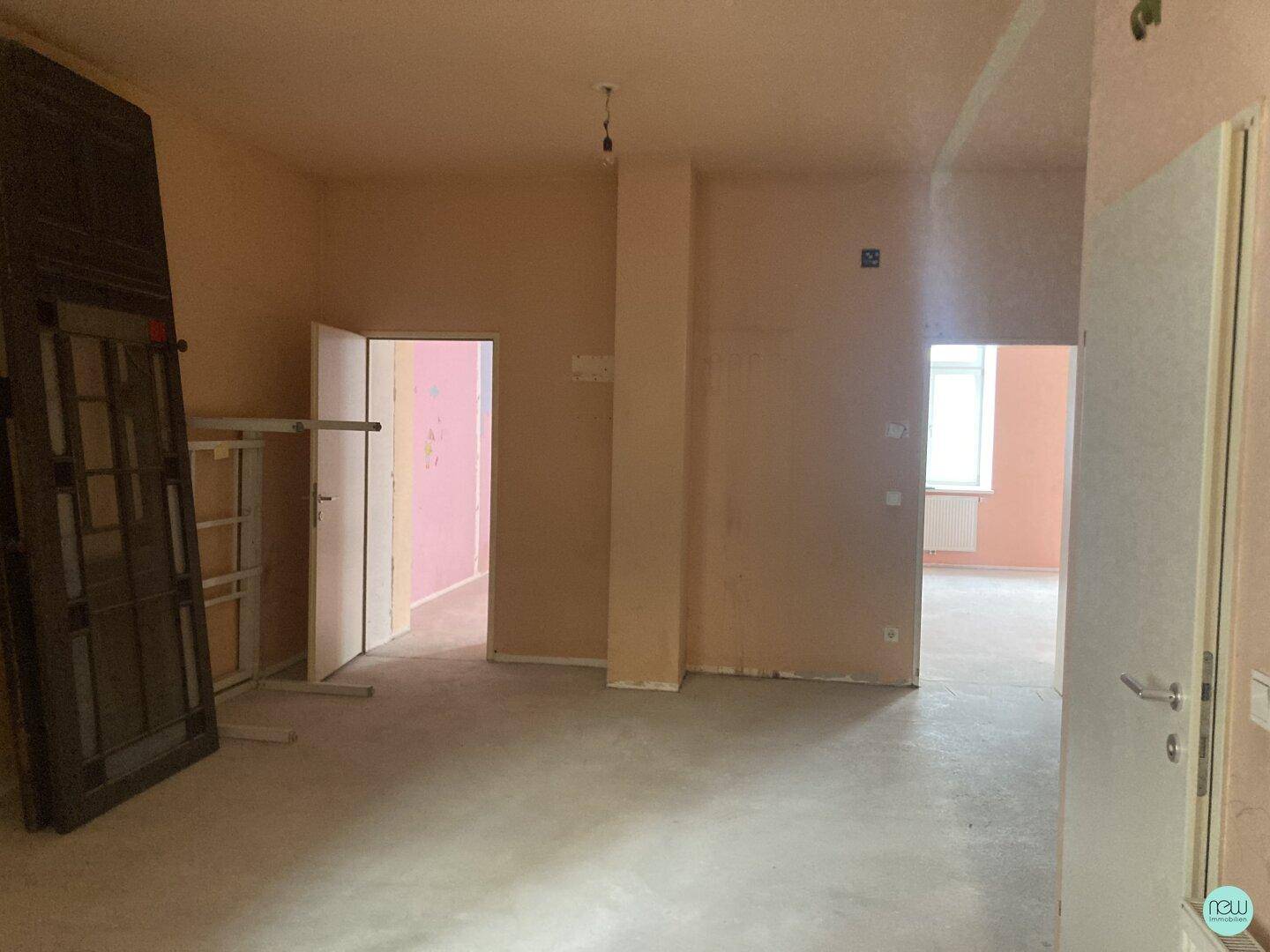 Unfertiger Innenraum mit mehreren Türen und einem großen, dunklen Element an der Wand, bereit zur Renovierung.