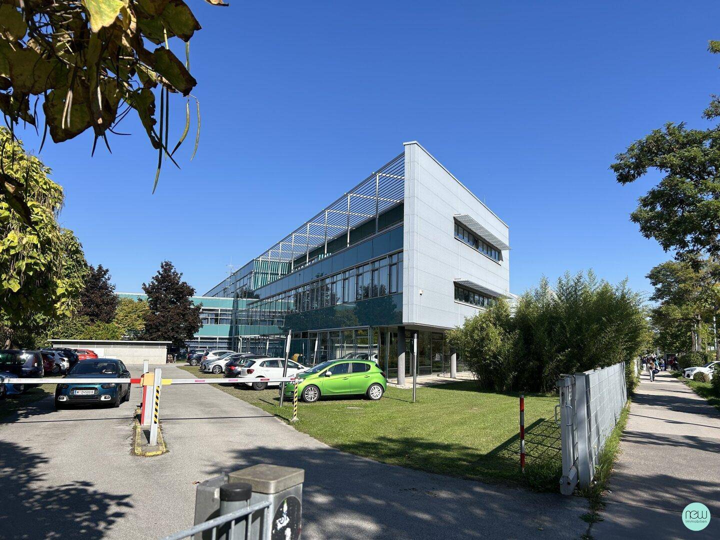 Modernes Bürogebäude mit Glasfassade, umgeben von Grünflächen und Parkplätzen.