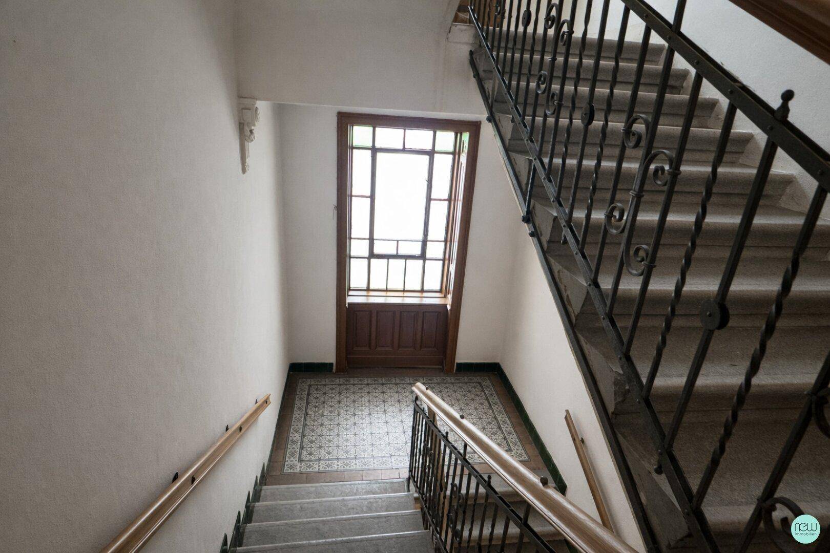 Historisches Treppenhaus mit Marmorstufen, schmiedeeisernem Geländer und gemusterten Fliesen im Eingangsbereich.