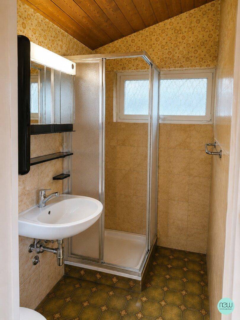 Funktionales Badezimmer mit Duschkabine, Einzelwaschbecken, Fliesen und Fenster für Tageslicht.