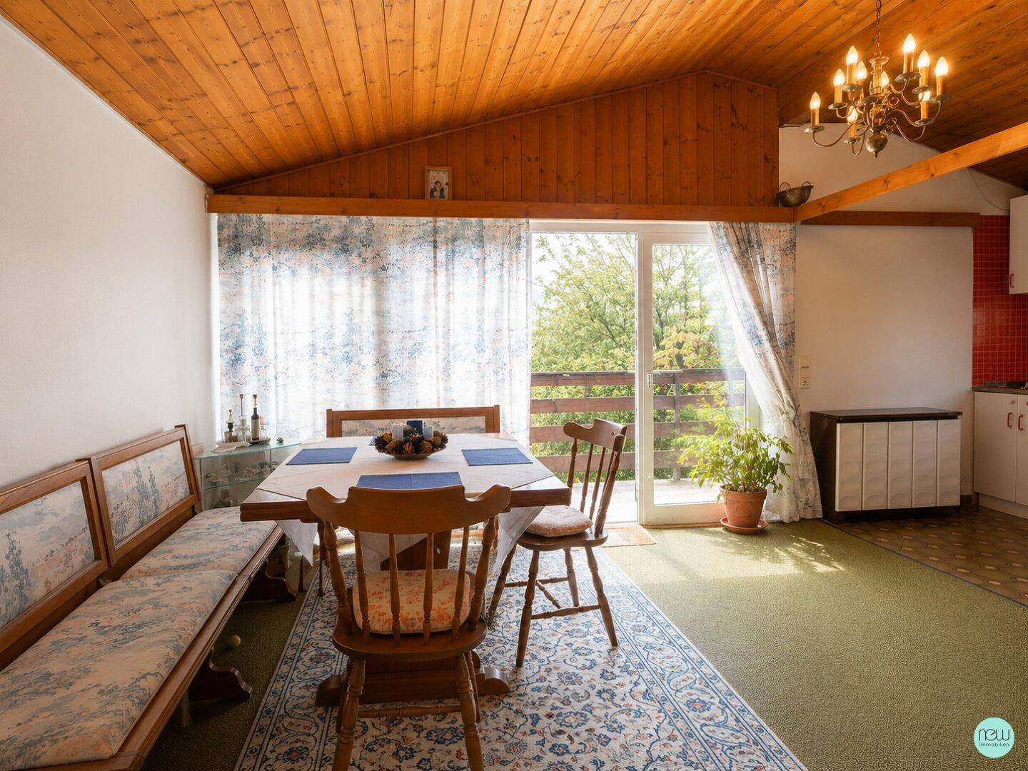 Gemütlicher Wohn-Essbereich mit Holzbalkendecke, Teppichboden und Zugang zum Außenbereich.