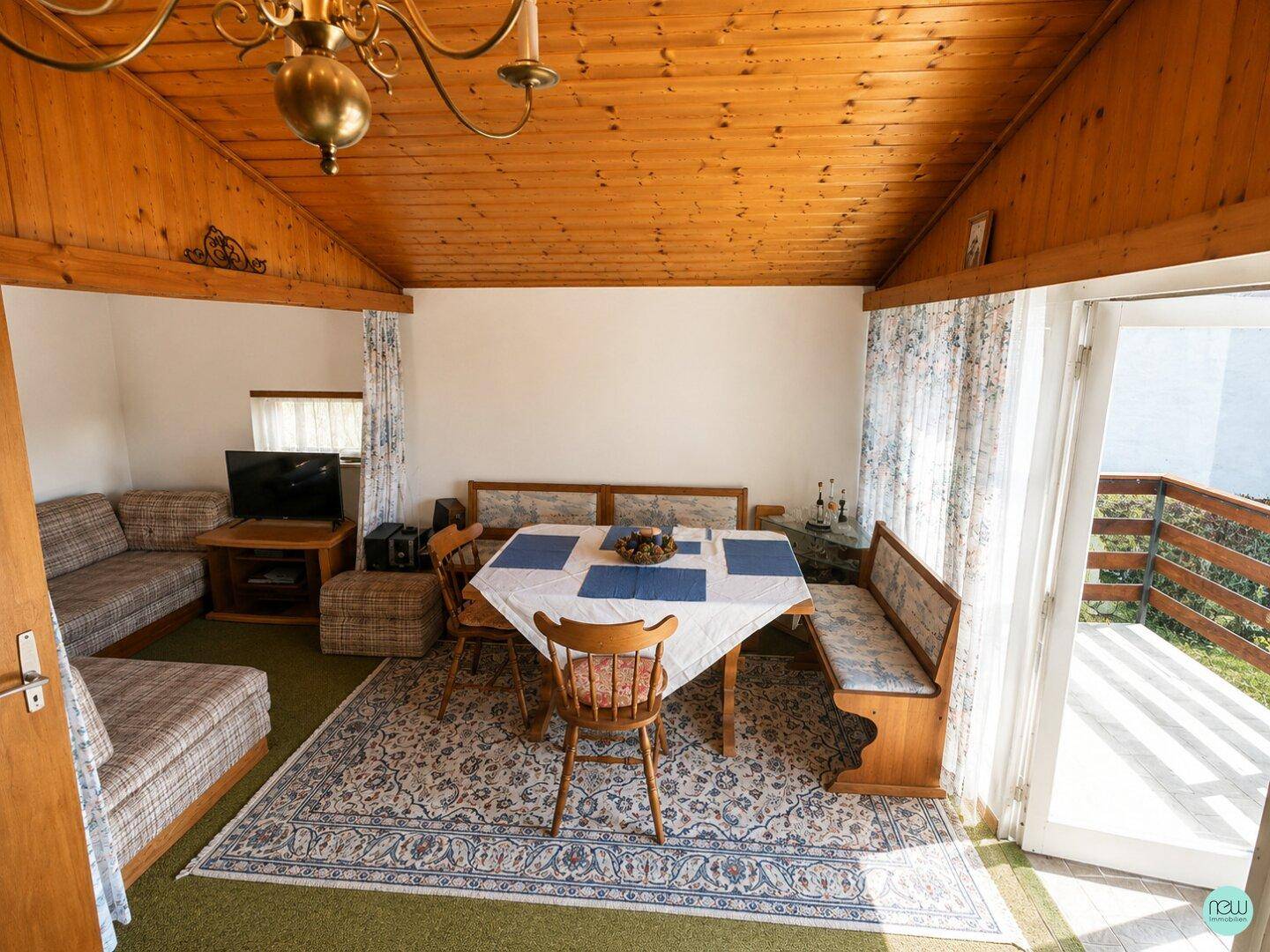 Heller Wohn- und Essbereich mit Holzbalkendecke, gemütlicher Sitzecke und Zugang zum Balkon.