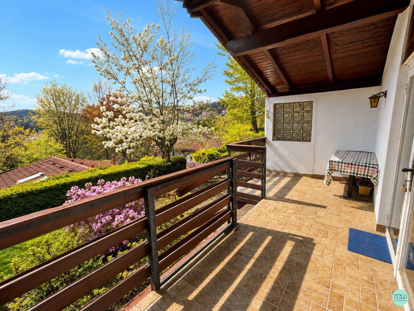 Geräumiger Balkon mit Fliesenboden und Holzgeländer, bietet einen weiten Blick ins Grüne.