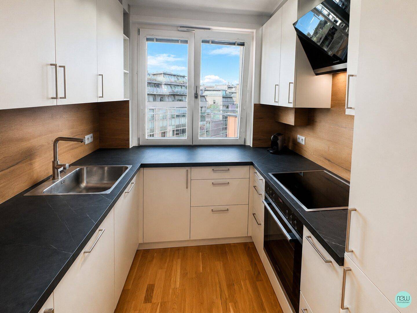 Moderne Küche mit weißen Schränken, dunklen Arbeitsplatten, Holzakzenten und einem Fenster mit Stadtblick.