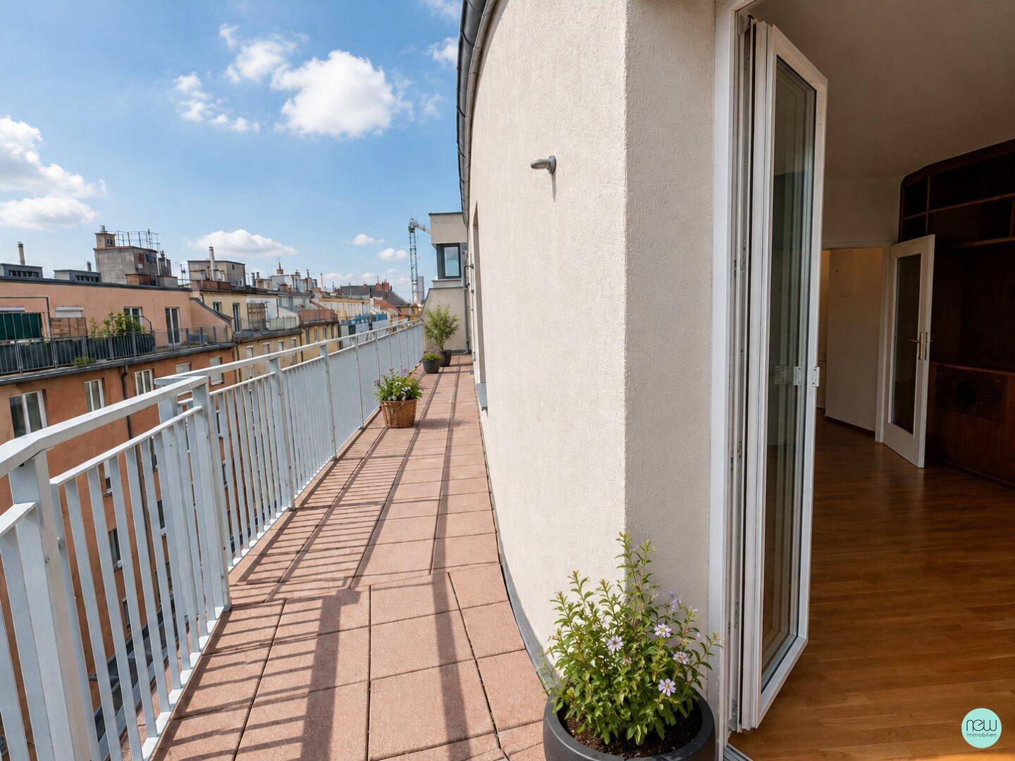 Geschwungener Balkon mit Fliesenboden, Pflanzen und Zugang zu einem Innenraum, mit Stadtblick.
