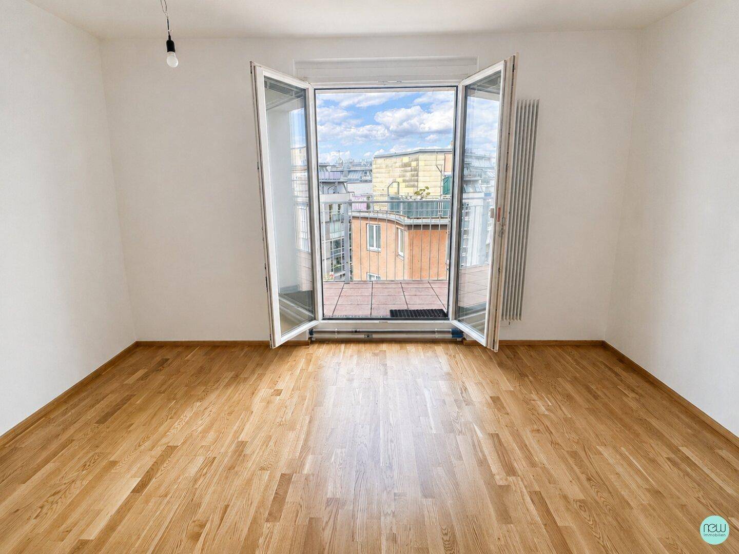 Helles Zimmer mit Parkettboden und großen Fenstertüren, die Zugang zu einem Außenbereich bieten.